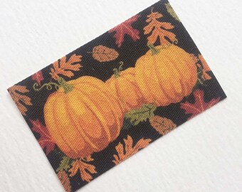 May include: A black fabric with a pattern of orange pumpkins and autumn leaves. The pumpkins are stacked on top of each other.