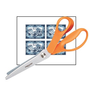 May include: Scissors with orange handles and a silver blade, featuring the text "FISKARS&reg; USA" on the blade. The scissors are positioned on top of a sheet of paper with four blue and white patterned squares.