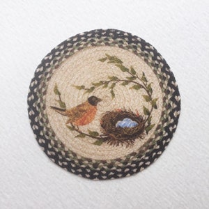 May include: Round jute rug with a black and green border. The center features a brown bird with orange breast sitting on a branch with green leaves. A brown nest with blue eggs is in the background.
