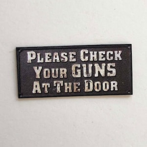 Letrero en miniatura de vaquero del oeste que dice: "Por favor, deje sus armas en la puerta"