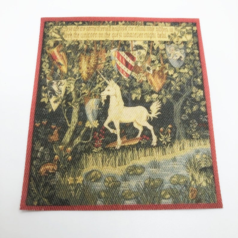 May include: A tapestry with a red border depicting a white unicorn standing in a forest with a stream and lily pads. The tapestry has text that reads "Where oft we are and sterially housed the round tower to give the unicorn on the quest si whatever might be found."