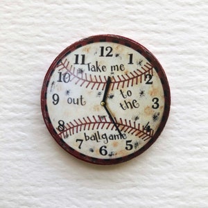 May include: A round, red and white baseball-themed clock with black hands. The clock face has the numbers 1-12, and the text "Take me out to the ballgame".