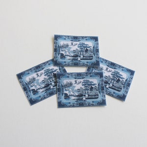 May include: Four blue and white fabric squares featuring a traditional Chinese design. The design depicts a landscape with a pagoda, trees, and birds.
