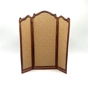 May include: A three-panel folding screen with a dark wood frame and a patterned fabric insert. The fabric has a tan background with a repeating pattern of small brown shapes. The top of each panel has a decorative, curved design.