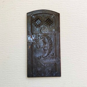 May include: A dark wooden door with intricate carvings, including a crescent moon with a face and clouds. The door has a metal hinge and a small keyhole.