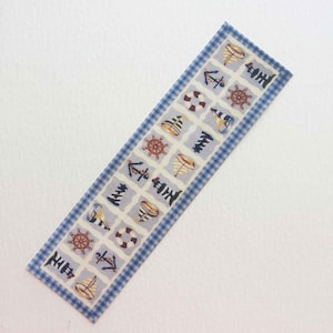 May include: A blue and white fabric ribbon with a nautical theme. The ribbon features a repeating pattern of anchors, sailboats, and steering wheels.