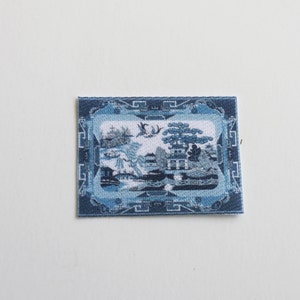 May include: Blue and white patterned rug with a traditional Chinese design. The rug has a blue border with a repeating geometric pattern.