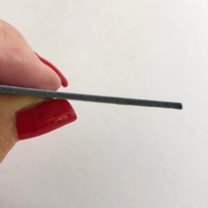 May include: A close-up of a gray, rectangular nail file.