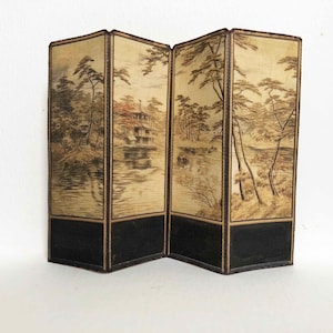 May include: A four-panel folding screen with a traditional Japanese landscape design. The screen is made of fabric with a beige background and black and brown ink drawings of trees, a lake, and a house. The screen has a black wooden frame.