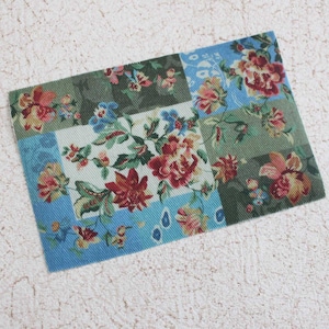 May include: A patchwork fabric with a floral pattern in shades of red, green, blue, and white. The fabric is made of a soft, textured material.