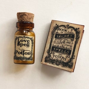 Op de afbeelding: Een klein glazen flesje met een kurkstop en een etiket met de tekst "Love Spell Potion". Het flesje ligt naast een klein boekje met een etiket met de tekst "Book of Spells and Potions".