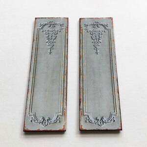 May include: Two decorative wall panels with a distressed, light blue paint finish. Each panel features an ornate, raised design in the center and a decorative border.
