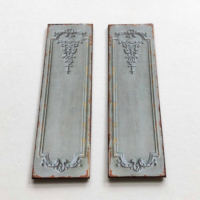 May include: Two decorative wall panels with a distressed, light blue paint finish. Each panel features an ornate, raised design in the center and a decorative border.