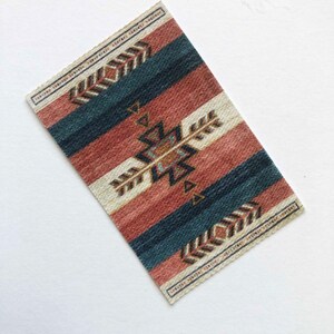 May include: A small, rectangular rug with a geometric pattern in shades of red, blue, and white. The rug has a fringed edge and a woven texture.