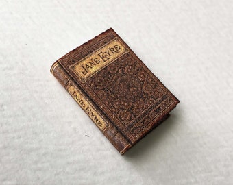 May include: A small, brown, leather-bound book with gold lettering on the spine and cover. The title of the book is "Jane Eyre".