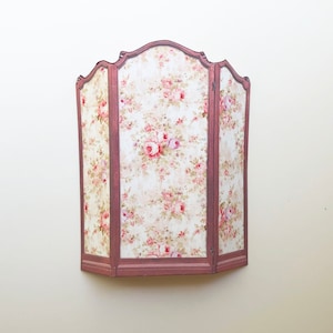 May include: A three-panel room divider with a floral pattern. The divider is made of wood and has a pink finish. The floral pattern is pink, white, and green.
