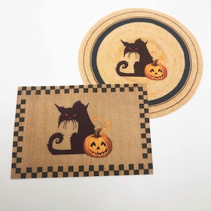 May include: Two Halloween-themed placemats. One is rectangular with a black and white checkered border. The other is round with a black border. Both feature a black cat silhouette with a jack-o'-lantern.