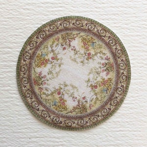 May include: A round, cream-colored rug with a floral pattern and a brown and green border. The rug has a vintage look and would be perfect for a dollhouse or miniature setting.