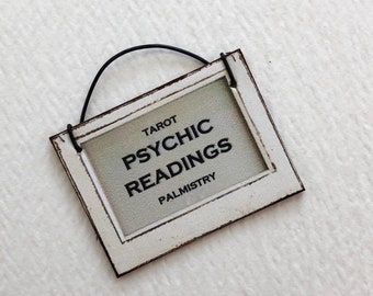 May include: White sign with black text that reads "Tarot Psychic Readings Palmistry". The sign has a black wire hanger.