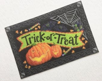 May include: A black and green doormat with a white spiderweb, orange pumpkins, and the text "Trick-or-Treat" on a green banner.
