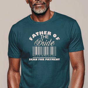 以下が含まれることがあります： ダークティールカラーの半袖Tシャツ。中央には白い文字で「FATHER OF THE BRIDE」と書かれ、その下にバーコードのグラフィックと「SCAN FOR PAYMENT」という文字がプリントされています。クルーネックで、無地のコットン生地を使用したスタンダードなフィット感のTシャツです。