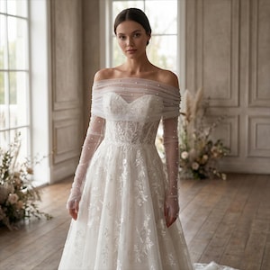 May include: A white off-the-shoulder wedding dress with long, sheer sleeves. The bodice features intricate lace detailing, and the neckline is adorned with small pearls. The dress has a full skirt and a flowing train, perfect for a bride.