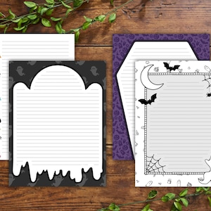 May include: A collection of Halloween-themed stationery. Includes lined notepaper with decorative borders featuring bats, ghosts, pumpkins, and other spooky elements. The stationery is set against a wooden background with green foliage.