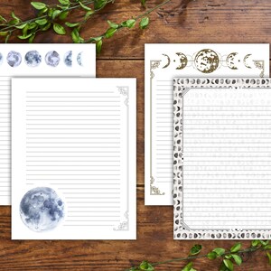 Op de afbeelding: Wit gelijnd briefpapier met hemelse maanfase-ontwerpen. Het briefpapier bevat aquarel illustraties van de maanfasen, met decoratieve randen en hoekaccenten. Het papier is gerangschikt op een houten oppervlak met groen.