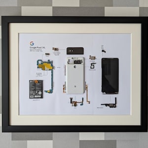 May include: Framed print of a deconstructed Google Pixel 2 XL smartphone, showcasing its internal components. The image includes the phone's screen, battery, and circuit boards, with the Google logo visible. The frame is black with a white mat.