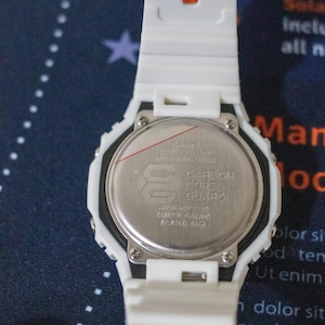 May include: A white digital watch with a white band. The watch face is silver with black text and a logo. The back of the watch has text that reads "CARBON CORE GUARD".