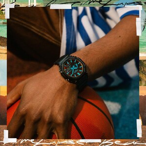 May include: Black wristwatch with a square face and a black band. The watch face has blue and red accents. The watch is on a person's wrist, with a basketball in the background.