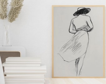 Può includere: Un bozzetto a matita incorniciato di una persona con cappello e vestito, vista da dietro. L'opera d'arte è in una cornice di legno chiaro ed è esposta su una parete di colore chiaro. Una pila di libri bianchi e un vaso con piante secche sono in primo piano.