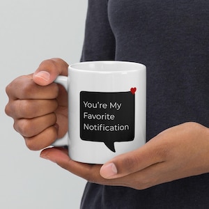 Può includere: Tazza in ceramica bianca con la scritta "You're My Favorite Notification" in un fumetto nero e un piccolo cuore rosso. La tazza è tenuta da una persona.
