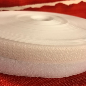 May include: A roll of white hook and loop fastener tape. The tape is rolled up and the hook side is facing the camera. The loop side is visible on the bottom of the roll.