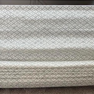 May include: A Roman shade with a repeating white and gray diamond pattern. The shade is made of fabric and is folded in horizontal pleats. The shade is mounted on a black bar.