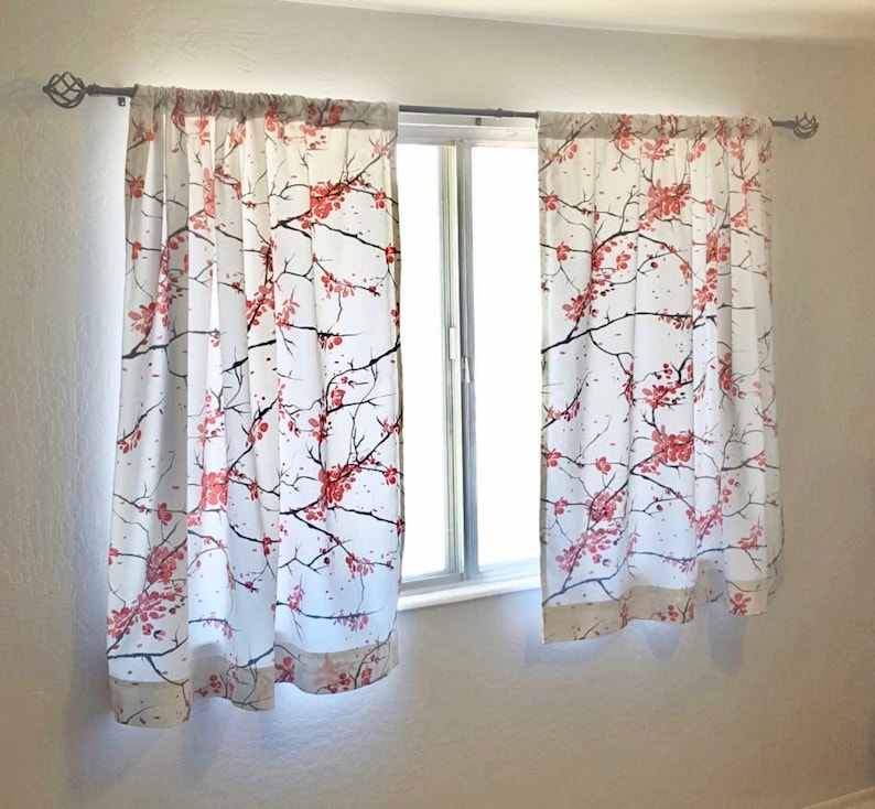 May include: White sheer curtains with a floral pattern of pink cherry blossoms on a white background. The curtains are hung on a window with a white trim.