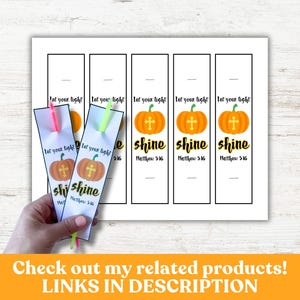 May include: White bookmarks with a pumpkin and cross design, the words "shine" and "Matthew 5:16". The bookmarks have neon pink and green tassels. The image also shows a sheet of similar bookmarks.
