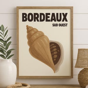 May include: A framed art print featuring a stylized seashell illustration in shades of brown and beige. The print includes the text "BORDEAUX SUD OUEST" in bold, dark brown lettering. The artwork is displayed in a wooden frame.