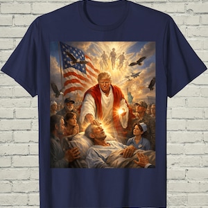 May include: Navy blue t-shirt featuring a detailed graphic. The graphic depicts a religious scene with an American flag, eagles, and figures in the clouds. A central figure is touching the head of a person lying down, surrounded by others.