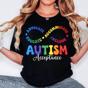 Puede incluir: Camiseta negra con la palabra "AUTISMO" en colores arcoíris y las palabras "ADVOCATE, EDUCATE, ACCOMMODATE, INCLUDE" en un patrón circular. La frase "Aceptación del Autismo" está escrita en blanco debajo.