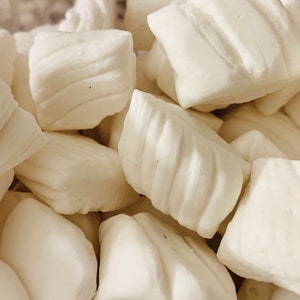 May include: A close-up of a bowl filled with white, individually wrapped, square-shaped candies.