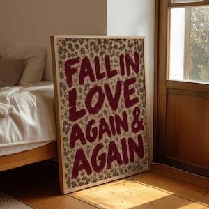 May include: A rectangular framed wall art piece featuring a light-coloured background with a dense, small-scale dark floral pattern. The text FALL IN LOVE AGAIN & AGAIN is printed in large, bold, dark red brushstroke-style capital letters.
