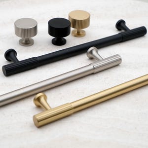 K&ouml;nnte beinhalten: Eine Sammlung von Schrankbeschl&auml;gen, darunter Kn&ouml;pfe und Griffe. Die Kn&ouml;pfe sind in Silber, Schwarz und Gold erh&auml;ltlich. Die Griffe sind in Schwarz, Silber und Gold erh&auml;ltlich. Alle Teile haben ein geripptes Design.