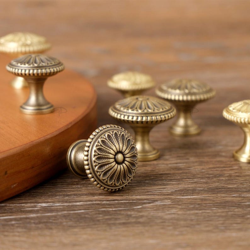 May include: Antique brass cabinet knobs with intricate floral designs. The knobs have a round shape with detailed patterns and a warm, aged finish. These decorative knobs are ideal for adding a vintage touch to furniture.