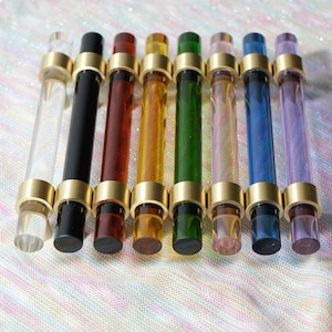 Peut inclure: Une collection de huit poignées de meubles colorées. Chaque poignée présente une tige cylindrique en verre clair ou coloré, accentuée par une quincaillerie en métal doré. Les couleurs incluent le transparent, le noir, le rouge, l'orange, le vert, le rose, le bleu et le violet.