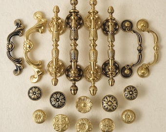 Puede incluir: Una colección de herrajes de gabinete de latón antiguo, que incluye manijas ornamentadas y perillas decorativas. Las manijas presentan intrincados diseños florales y de volutas, con acabados dorados y negros. Las perillas tienen varios patrones florales.