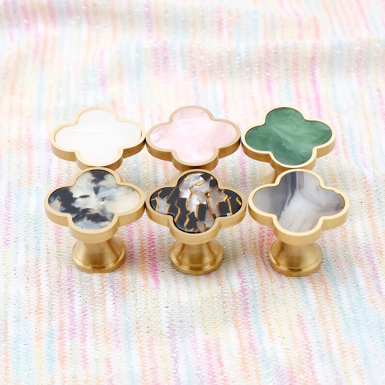 Op de afbeelding: Zes decoratieve kastknoppen met een klaverbladontwerp. De knoppen hebben een gouden basis en bovenkanten in verschillende kleuren en patronen, waaronder wit, roze, groen en gemarmerde ontwerpen.