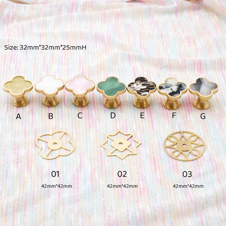 Op de afbeelding: Een verzameling decoratieve kastknoppen en -grepen in verschillende ontwerpen en kleuren. De knoppen hebben klavervormige toppen met goudkleurige bases. De afbeelding bevat ook goudkleurige decoratieve accenten. De tekst geeft de grootte van de knoppen aan.