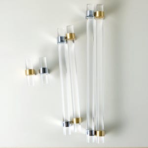 Puede incluir: Tiradores y manijas de gabinete de acrílico transparente con detalles metálicos dorados y plateados. El hardware está disponible en varias longitudes y tamaños, adecuado para cajones y gabinetes. El diseño moderno presenta una forma cilíndrica.