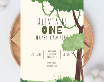 May include: A cream-colored invitation with a forest theme. The text reads "Olivia is One Happy Camper!" with event details. Green trees and foliage frame the text. The invitation is on a wooden plate with a brown envelope.